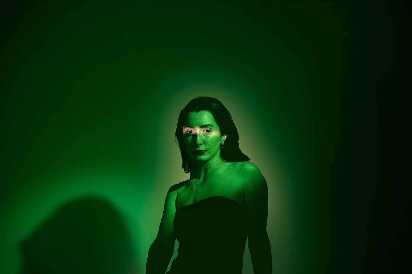 A woman's portrait bathed entirely in green light, looking off to the side against a plain backdrop.
